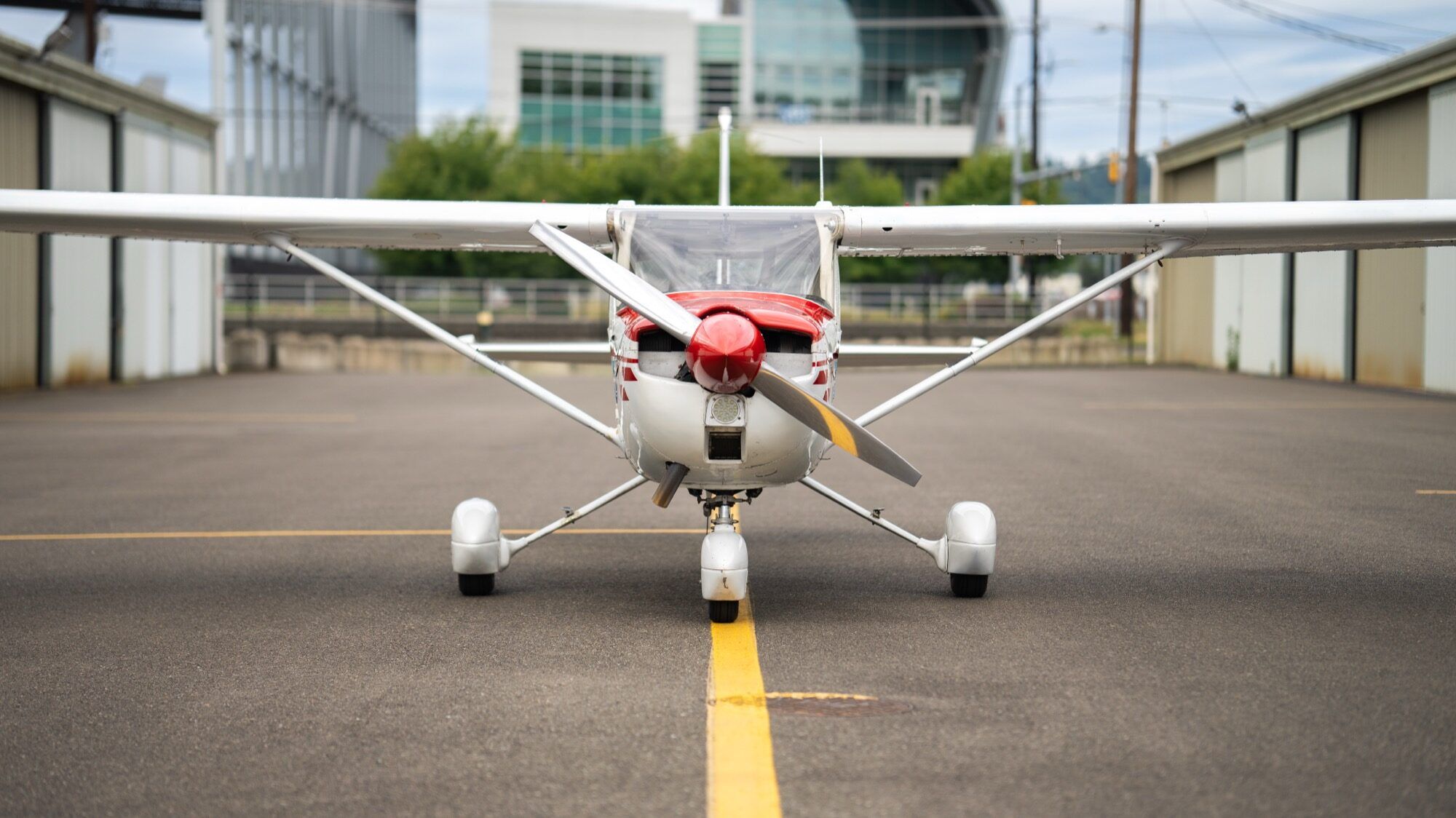 Red, white and blue Cessna 150M head-on between two hangar rows