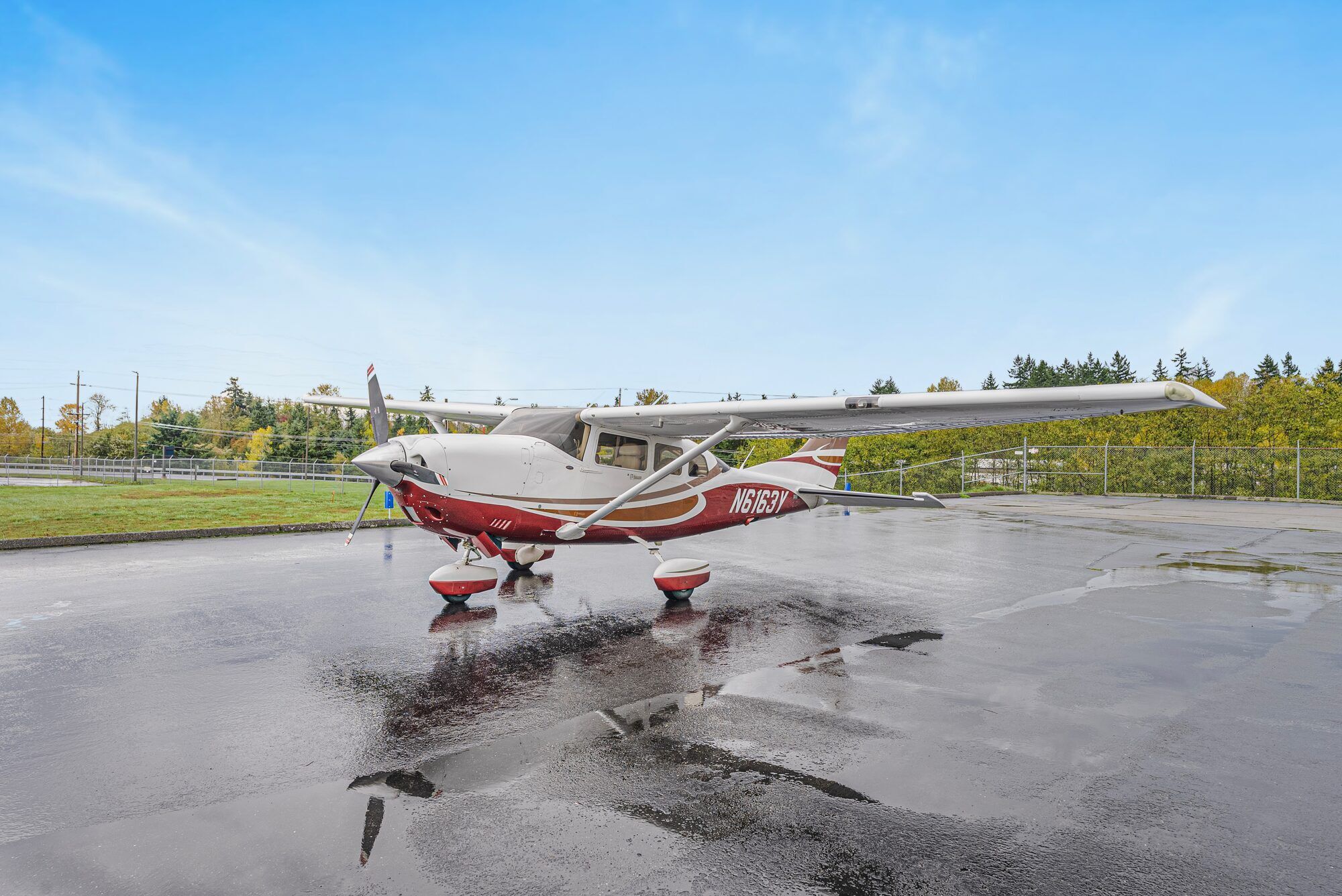 Maroon and white 2008 Cessna T206H Turbo Stationair parked on a wet ramp beside a hangar