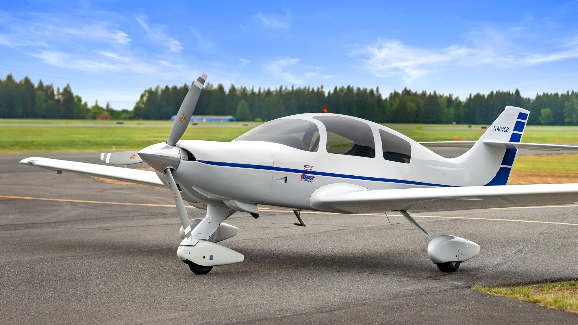White Wheeler Express experimental aircraft parked on a ramp beside a grass airfield